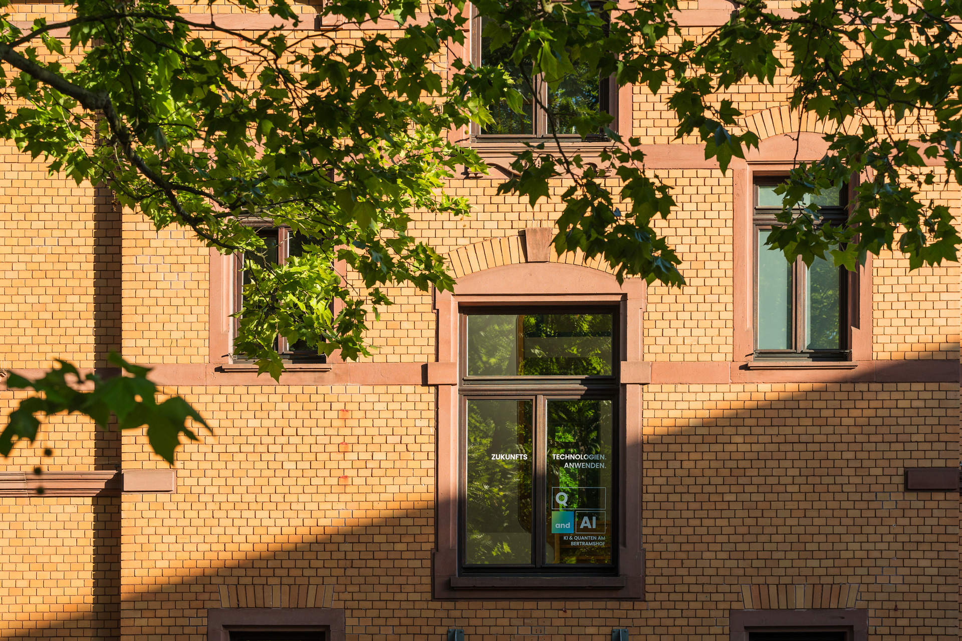Fensterbeschriftung „Zukunftstechnologien. Anwenden." mit Q and AI Logo an der historischen Backsteinfassade des Bertramshofs in Frankfurt